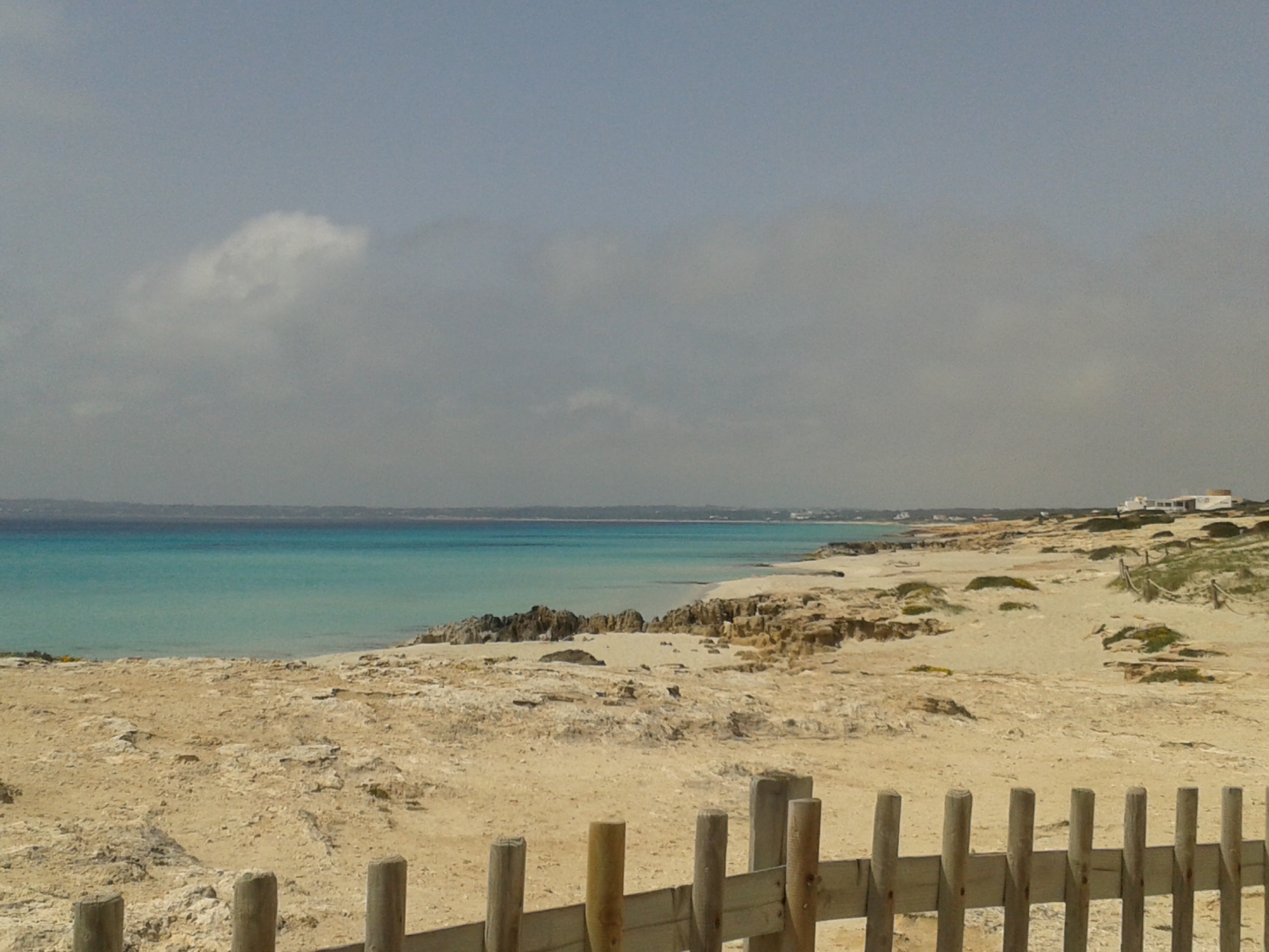Het lege zand van Platja de Migjorn op Formentera in april, met een houten hek in de duinen en turkoois water
