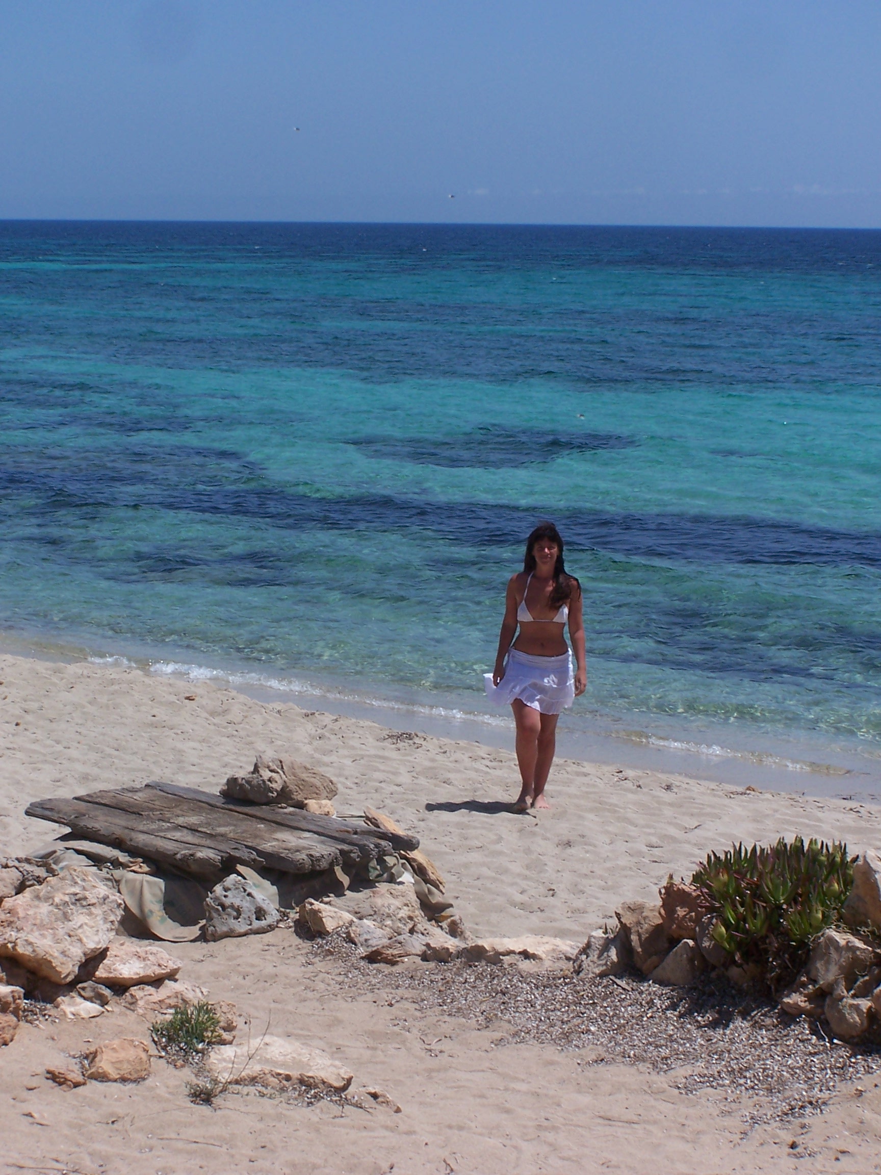 Formentera in juni: zeewater, lange dagen en het voertuigquotum 1 Vrouw loopt over het lege zand van Platja de Migjorn op Formentera met blauwgroen water erachter