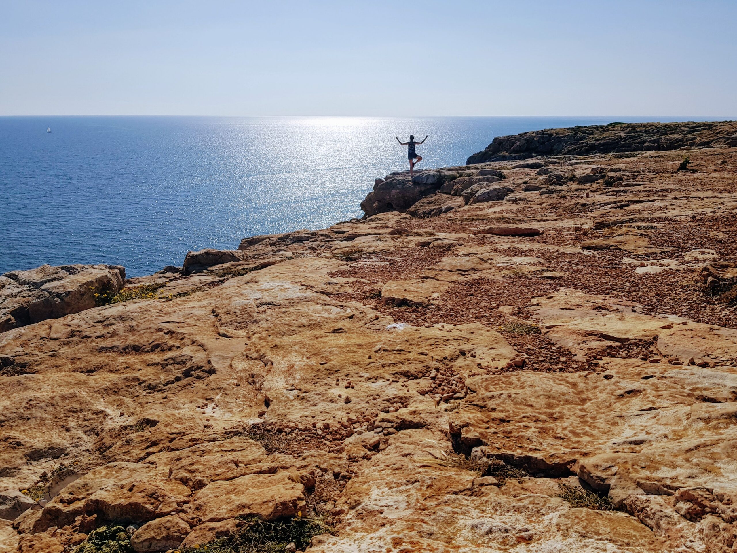 Het kale rotsplateau van Cap de Barbaria op Formentera met een enkele wandelaar aan de rand boven de blauwe zee