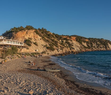 Het kiezelstrand van Cala d'Hort op Ibiza in april, met een handvol bezoekers en een bootje in het late middaglicht