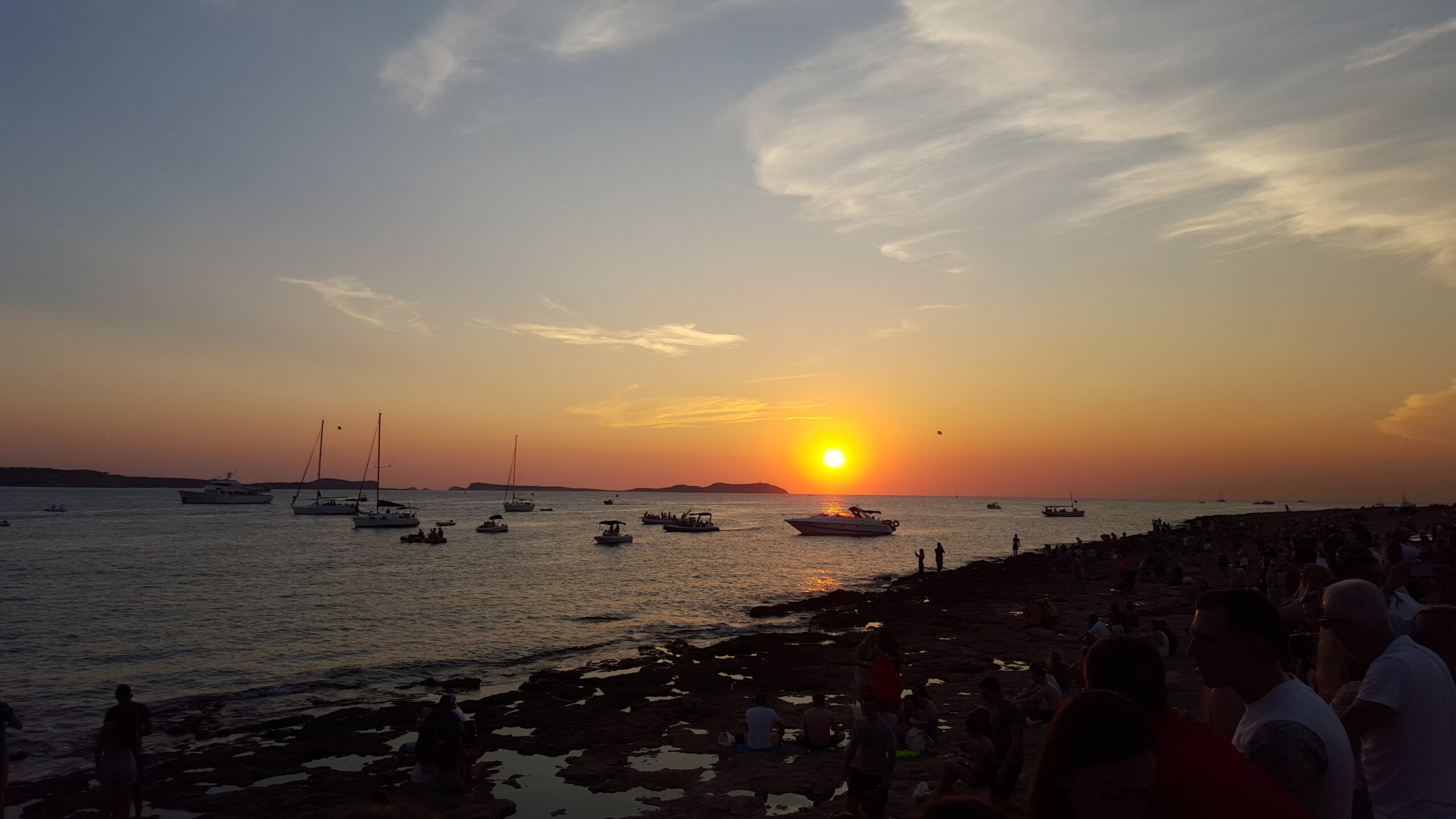 Ibiza in juli: de drukste en duurste maand van het jaar 1 Publiek op de rotsen bij de sunset strip van Sant Antoni op Ibiza terwijl de zon in zee zakt