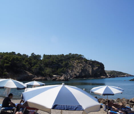 Parasols en ligbedden op het strand van Cala Xarraca op Ibiza bij kalme zee in juni