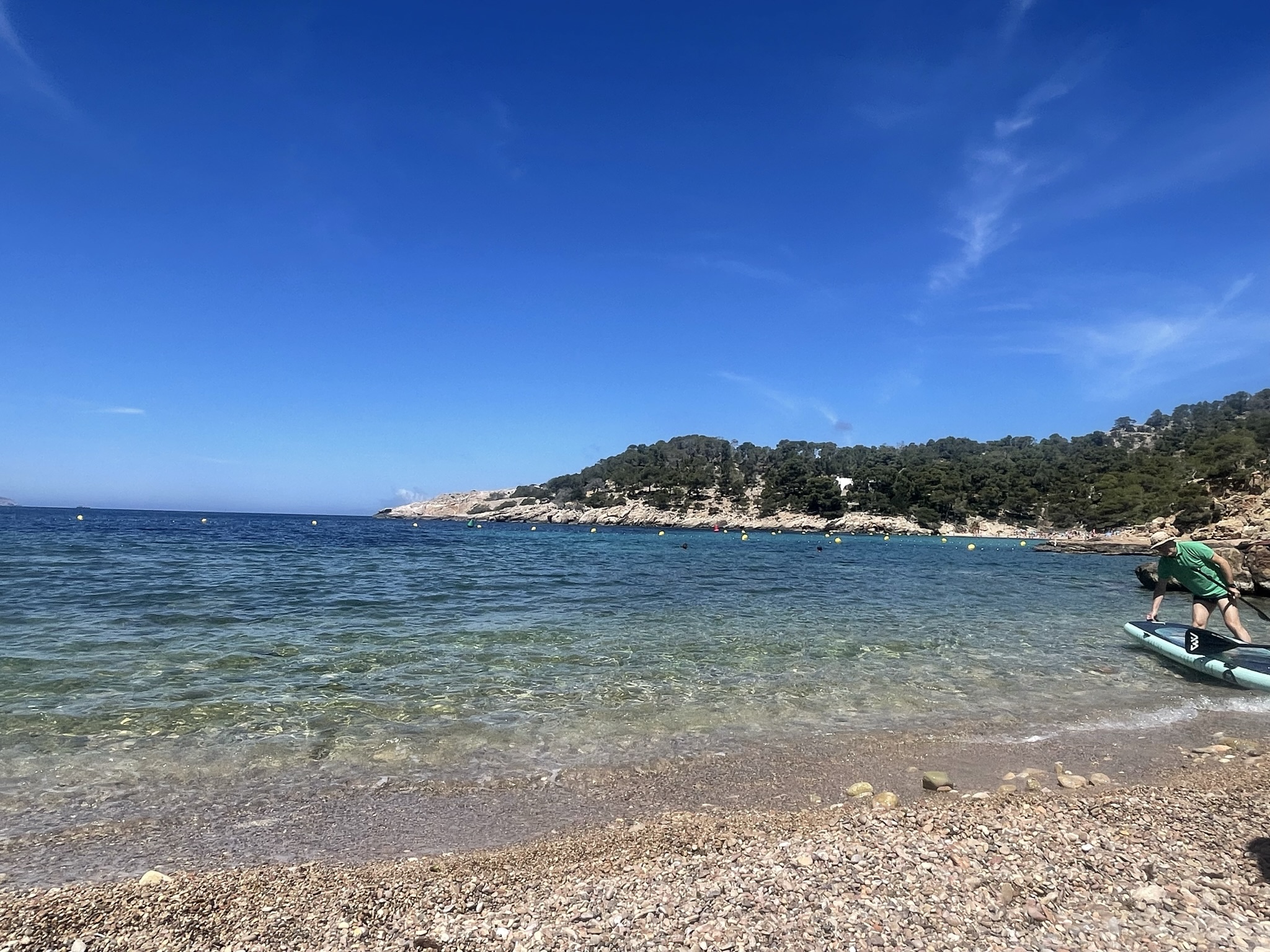 Ibiza in mei 2027: het seizoen opent en het water wordt zwembaar 1 Helder turquoise water en een kiezelstrand bij Cala Salada op Ibiza begin mei, met een suppende bezoeker