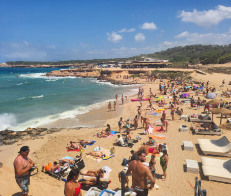Het strand van Platges de Comte op Ibiza met badgasten, ligbedden en turquoise water begin september