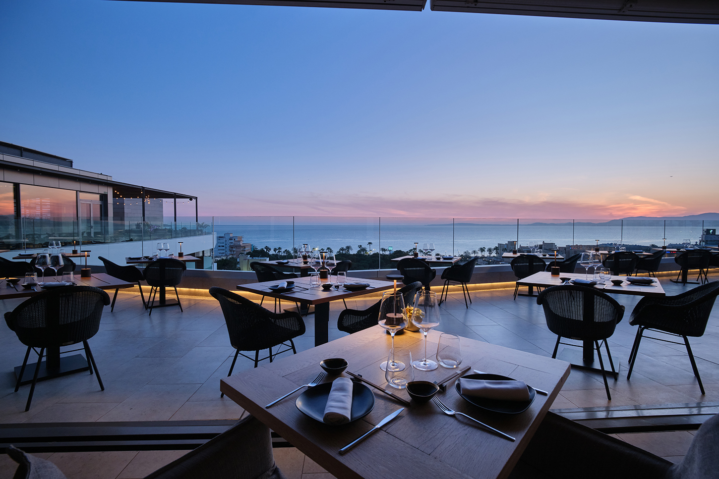Het dakterras van restaurant KATAGI Blau aan de Playa de Palma bij zonsondergang, met gedekte tafels en uitzicht over de baai van Palma
