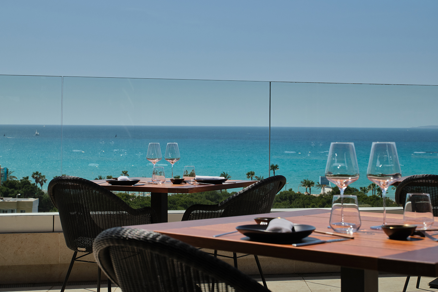 Gedekte tafels op het terras van KATAGI Blau achter een glazen balustrade, met de turquoise zee van de baai van Palma erachter