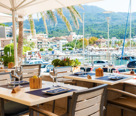 Gedekte tafels op het verhoogde terras van Kingfisher in Port de Sóller, met uitzicht over de jachthaven en de beboste berghelling erachter