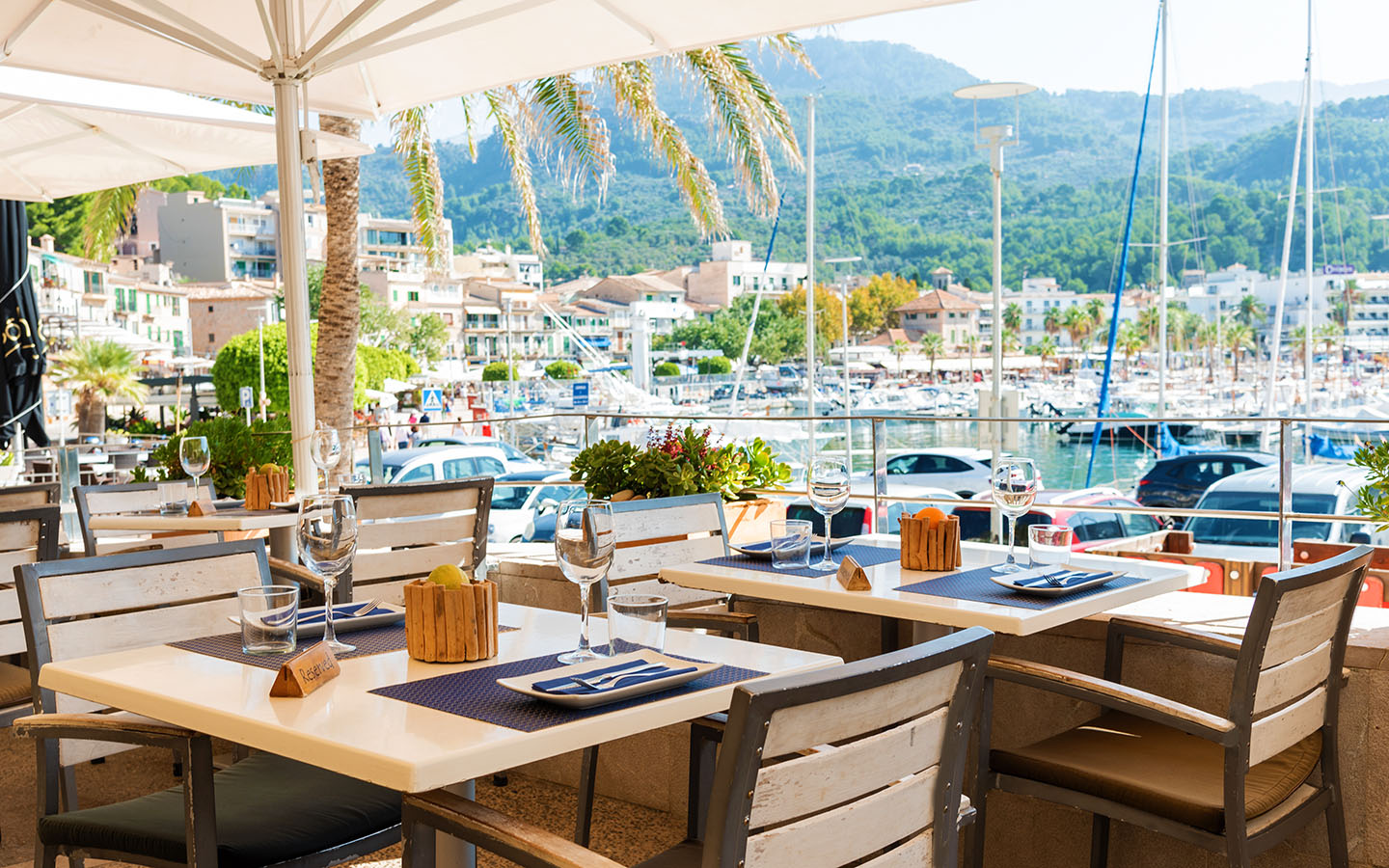 Kingfisher Port de Sóller: vis en zeevruchten boven de jachthaven 1 Gedekte tafels op het verhoogde terras van Kingfisher in Port de Sóller, met uitzicht over de jachthaven en de beboste berghelling erachter