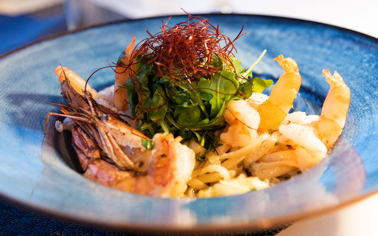 Kingfisher Port de Sóller: vis en zeevruchten boven de jachthaven 5 Pasta met gamba's en rucola in een blauw diep bord bij Kingfisher in Port de Sóller, afgewerkt met gedroogde chilidraden