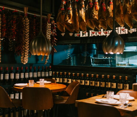 Eetzaal van La Bodeguilla in Palma met een rij hangende Iberische hammen boven de tafels en wanden vol wijnflessen