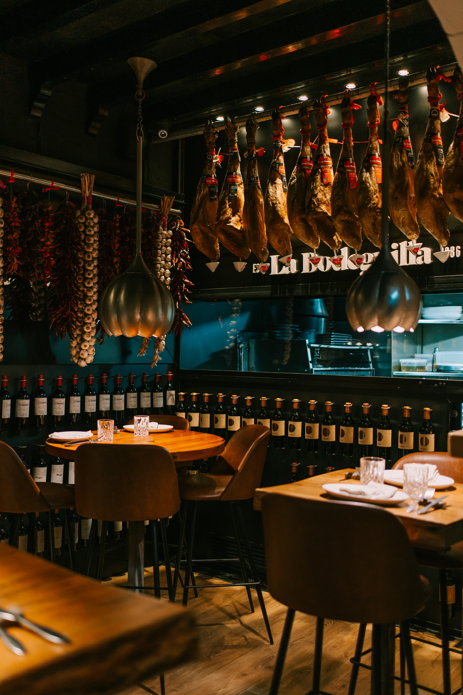 Eetzaal van La Bodeguilla in Palma met een rij hangende Iberische hammen boven de tafels en wanden vol wijnflessen