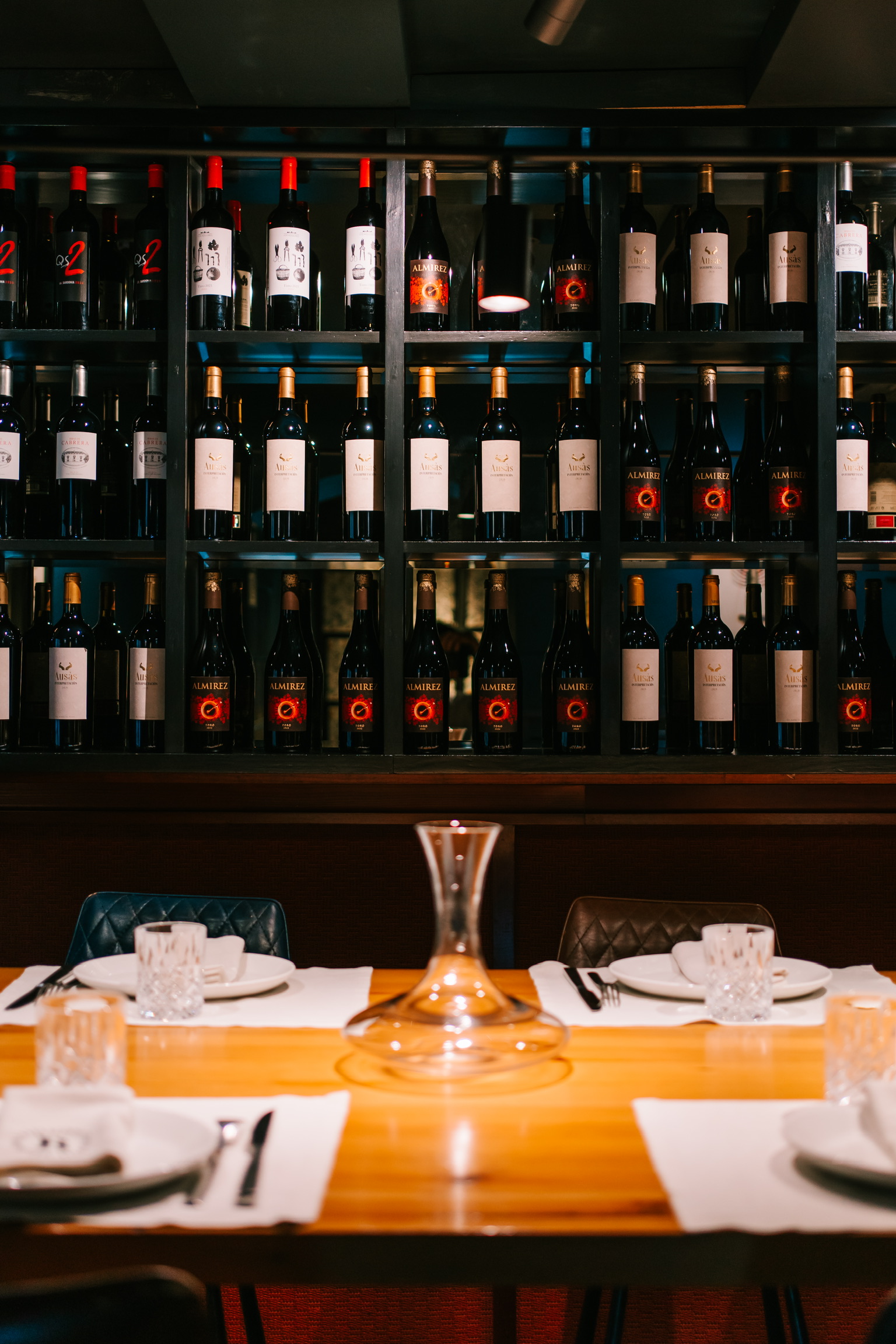 Gedekte tafel met karaf voor de verlichte wijnrekken in de eetzaal van La Bodeguilla in Palma