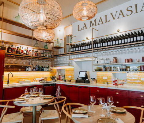 De binnenruimte van restaurant La Malvasia in Palma met gele tegels, bordeauxrode kasten, rieten lampen en de naam in grote letters boven de bar