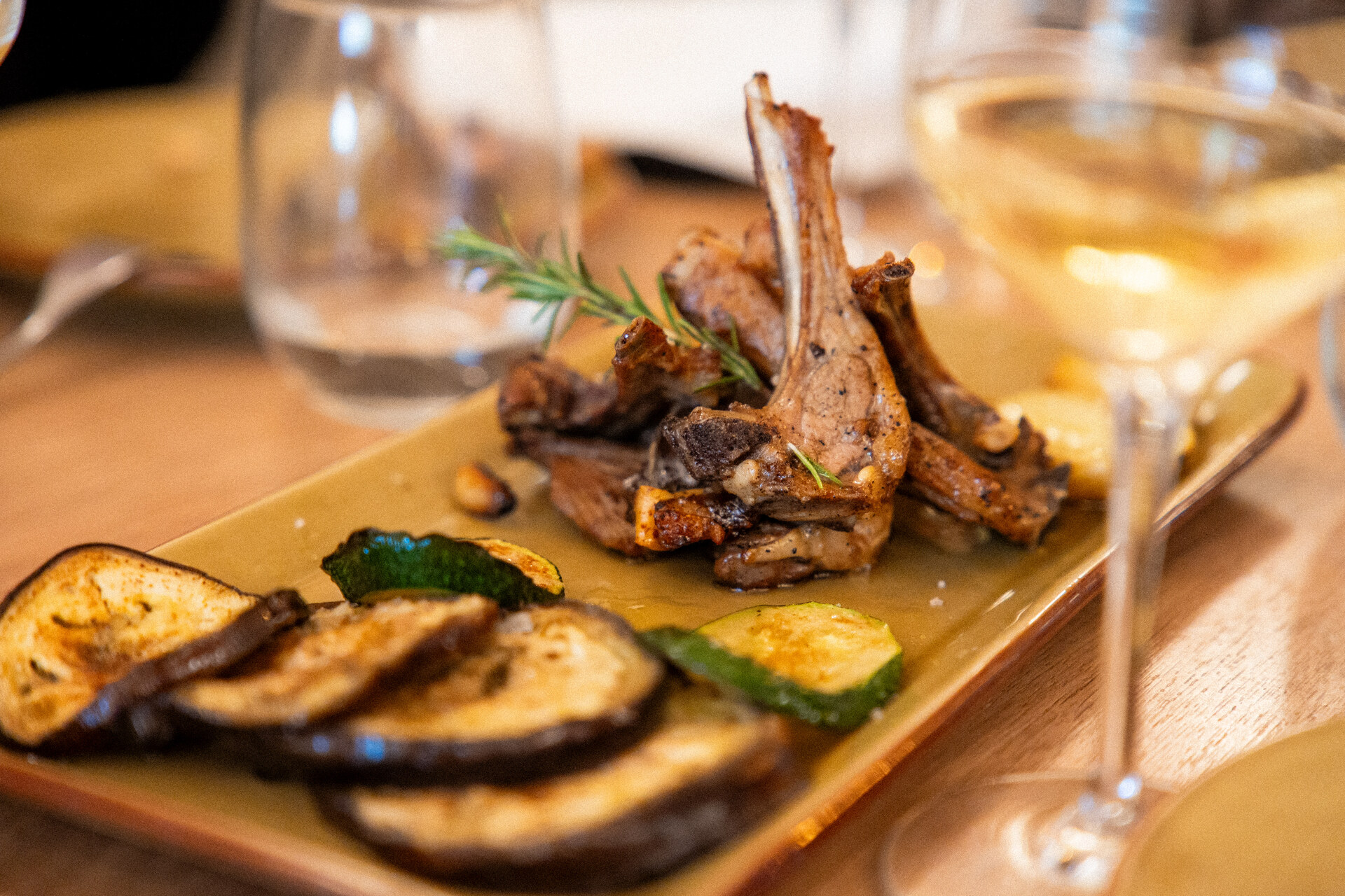 Gegrilde lamskoteletjes met rozemarijn, gegrilde aubergine en courgette op een geel bord bij La Malvasia