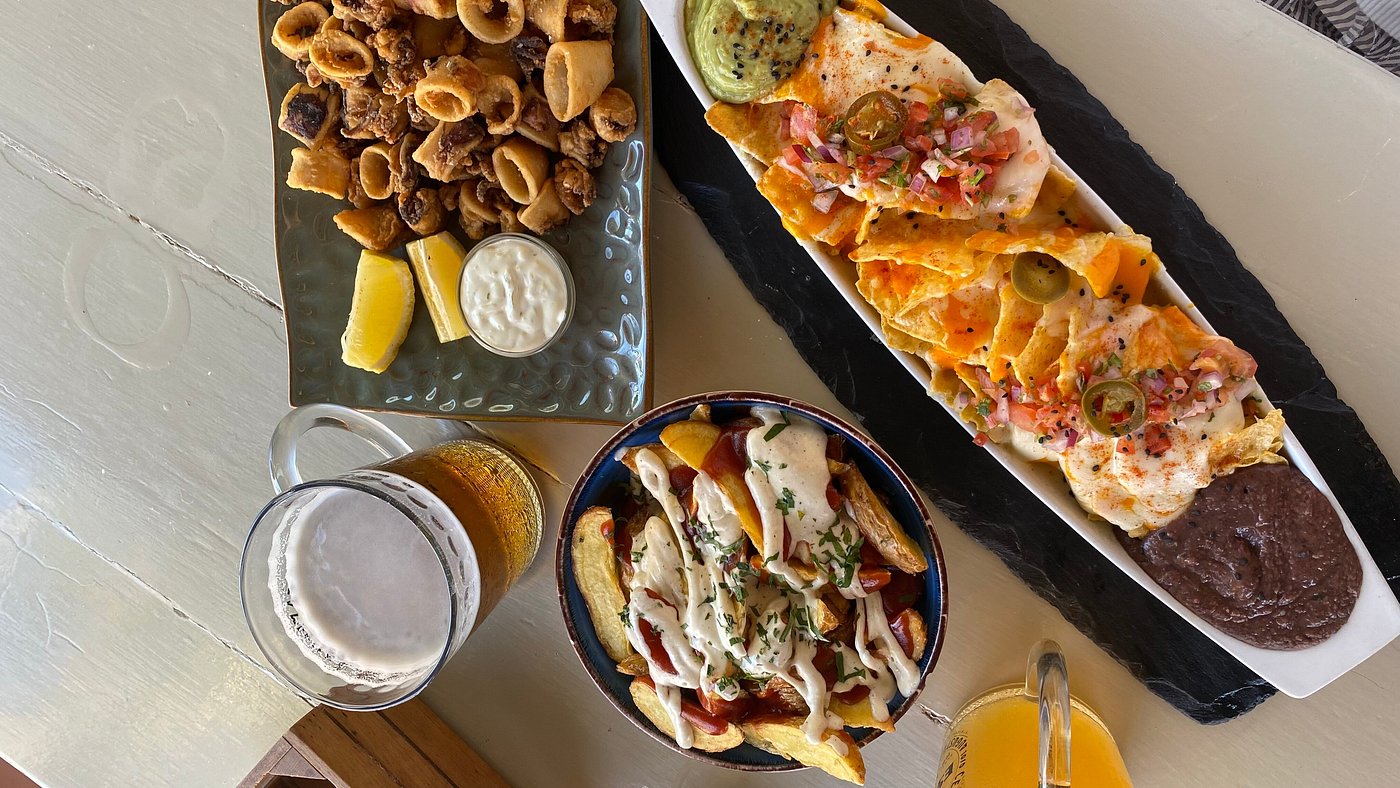L'Amorigen Ibiza: het beschilderde strandrestaurant van Cala Nova 8 Van bovenaf gefotografeerde deelgerechten bij L'Amorigen: een langwerpige pizza, nacho's met dips en een schaaltje olijven