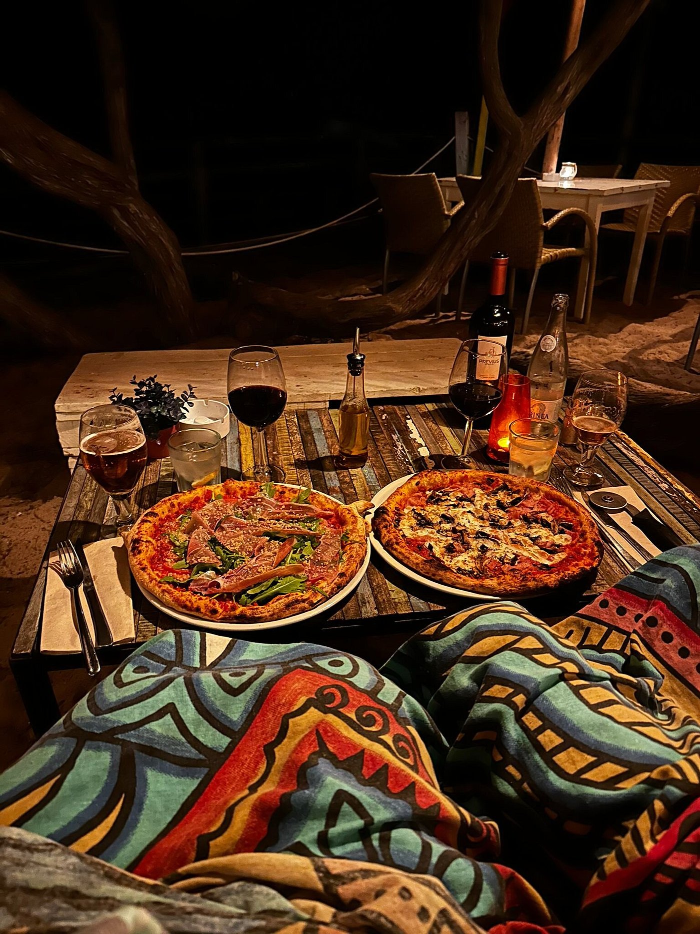 L'Amorigen Ibiza: het beschilderde strandrestaurant van Cala Nova 4 Twee pizza's uit de houtoven op een beschilderde tafel bij avondlicht, met glazen rode wijn ernaast