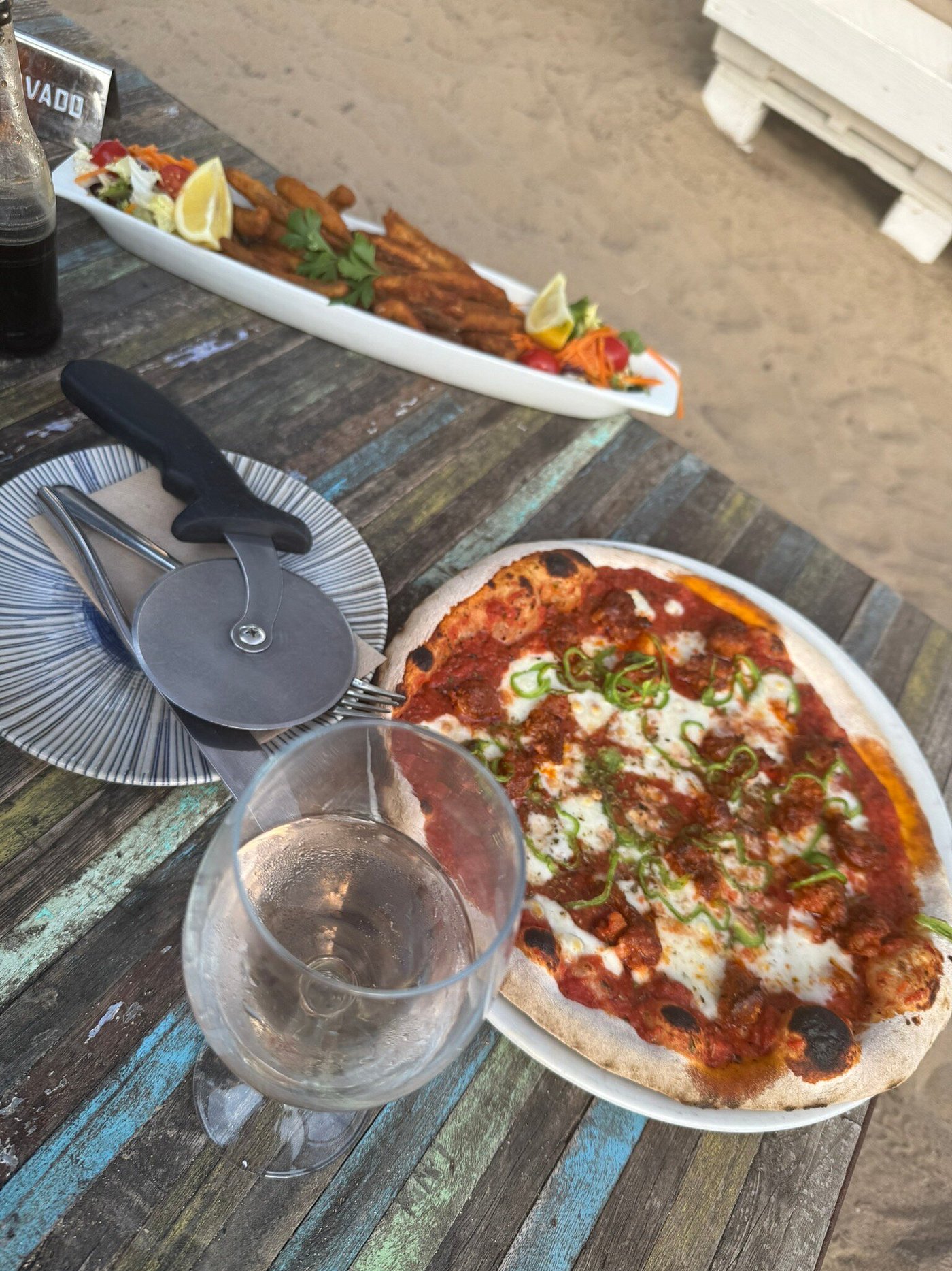 L'Amorigen Ibiza: het beschilderde strandrestaurant van Cala Nova 6 Een pizza met pizzasnijder en een glas rosé op de blauw beschilderde tafel van L'Amorigen