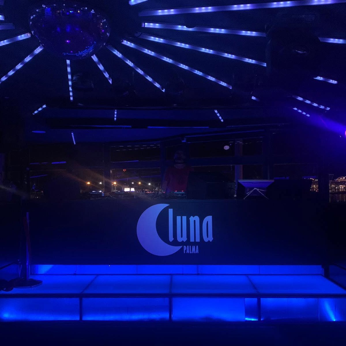 De lege dansvloer van Luna Palma in blauw licht, met discobal, lichtbruggen en het logo van de club op de wand