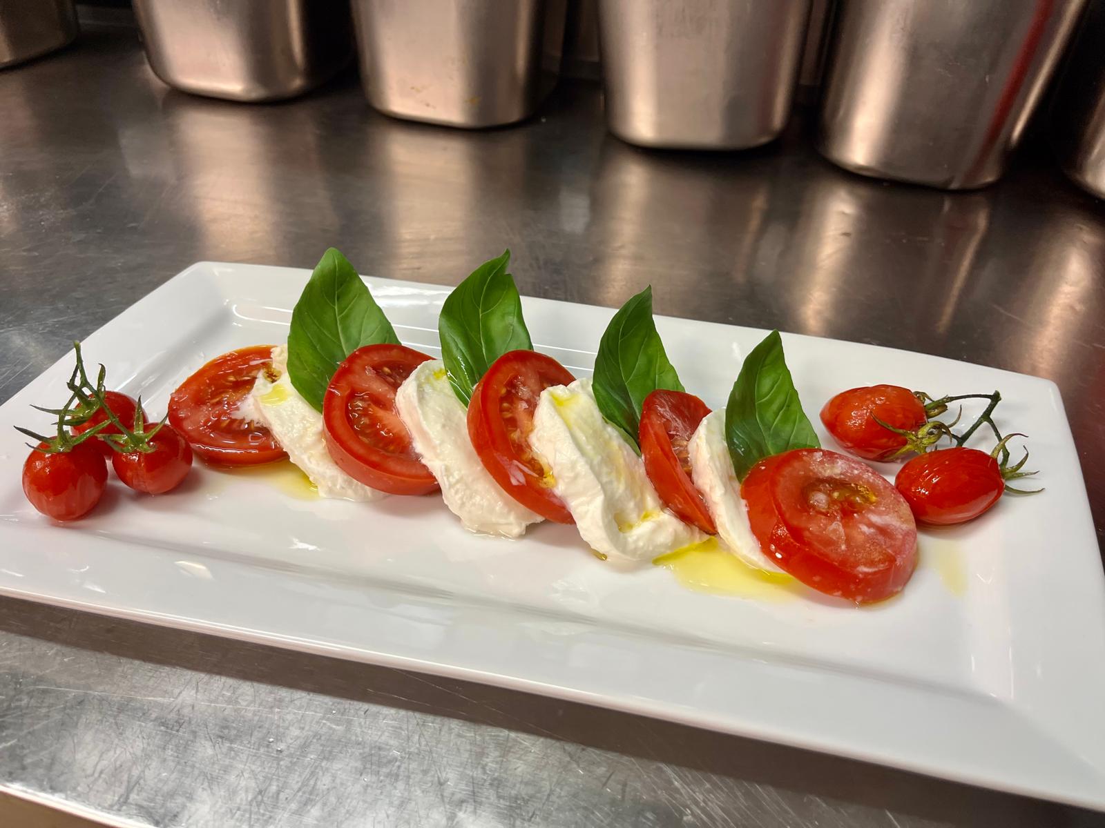 Caprese van buffelmozzarella met tomaat en basilicum op een wit bord in de keuken van Macondo