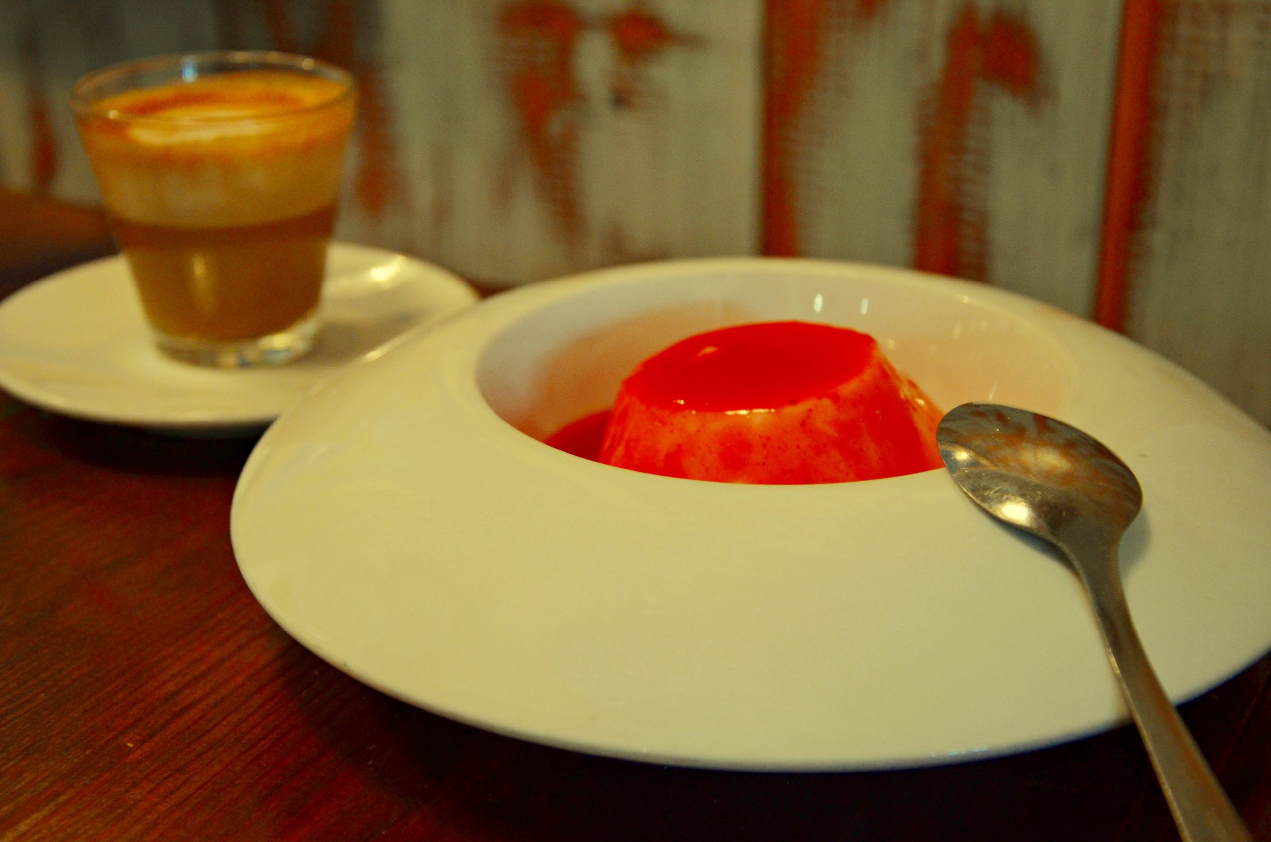 Flan met rode vruchtensaus en een cortado op de houten tafel van Macondo