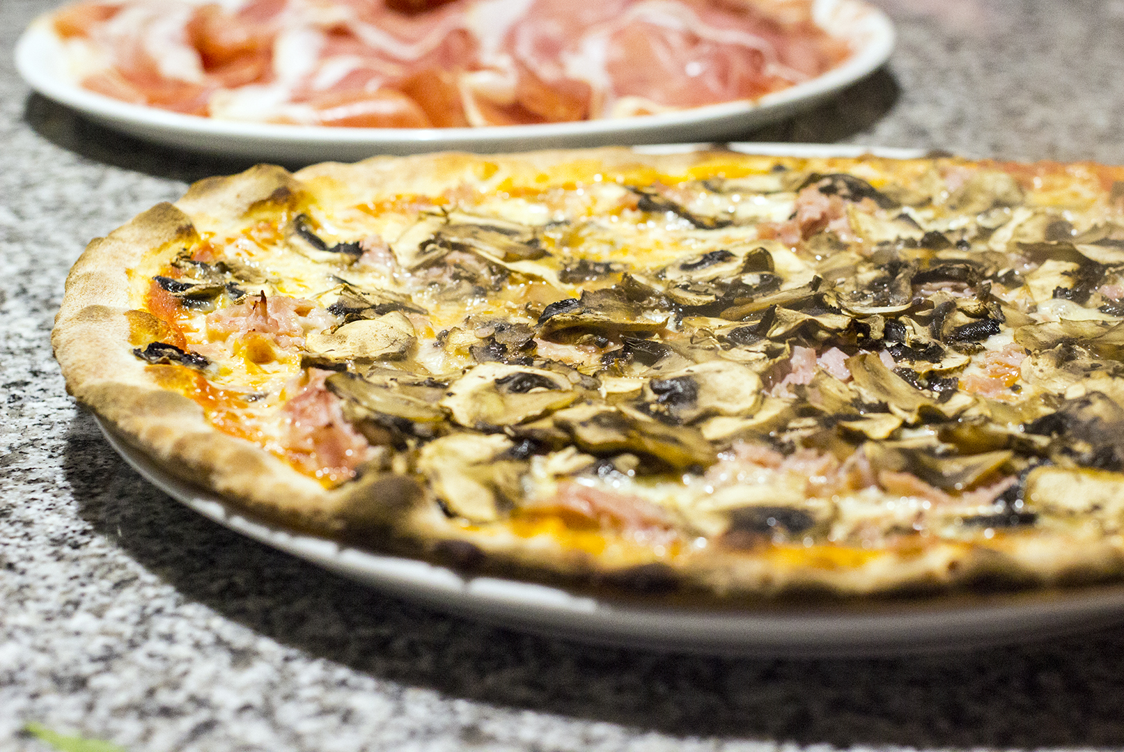 Dunne pizza met ham en champignons van Macondo, met een schaal prosciutto erachter