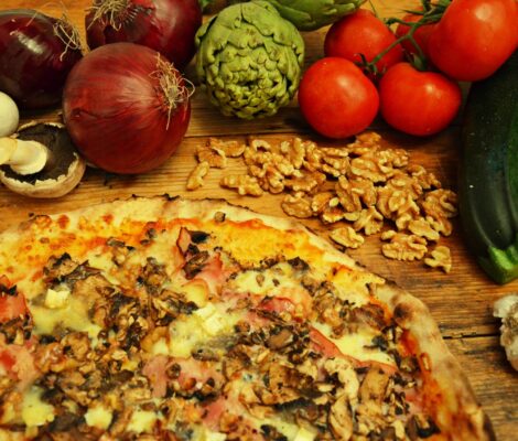 Dunne pizza van Macondo op Formentera op een houten tafel, omringd door verse uien, artisjokken, tomaten en knoflook