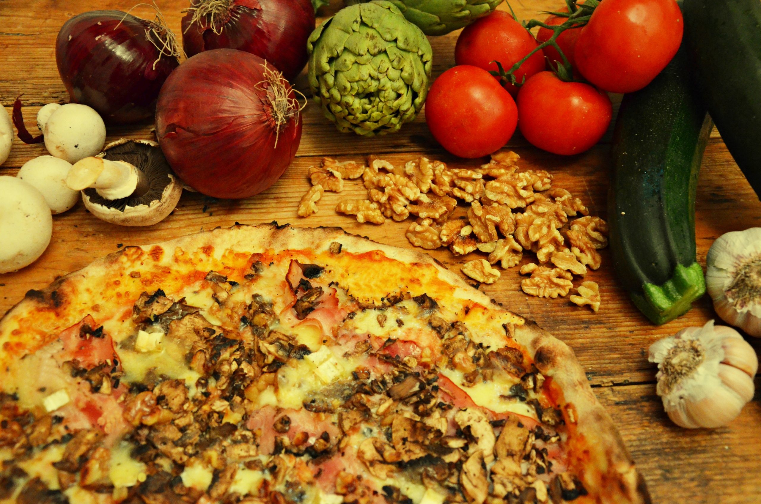 Dunne pizza van Macondo op Formentera op een houten tafel, omringd door verse uien, artisjokken, tomaten en knoflook