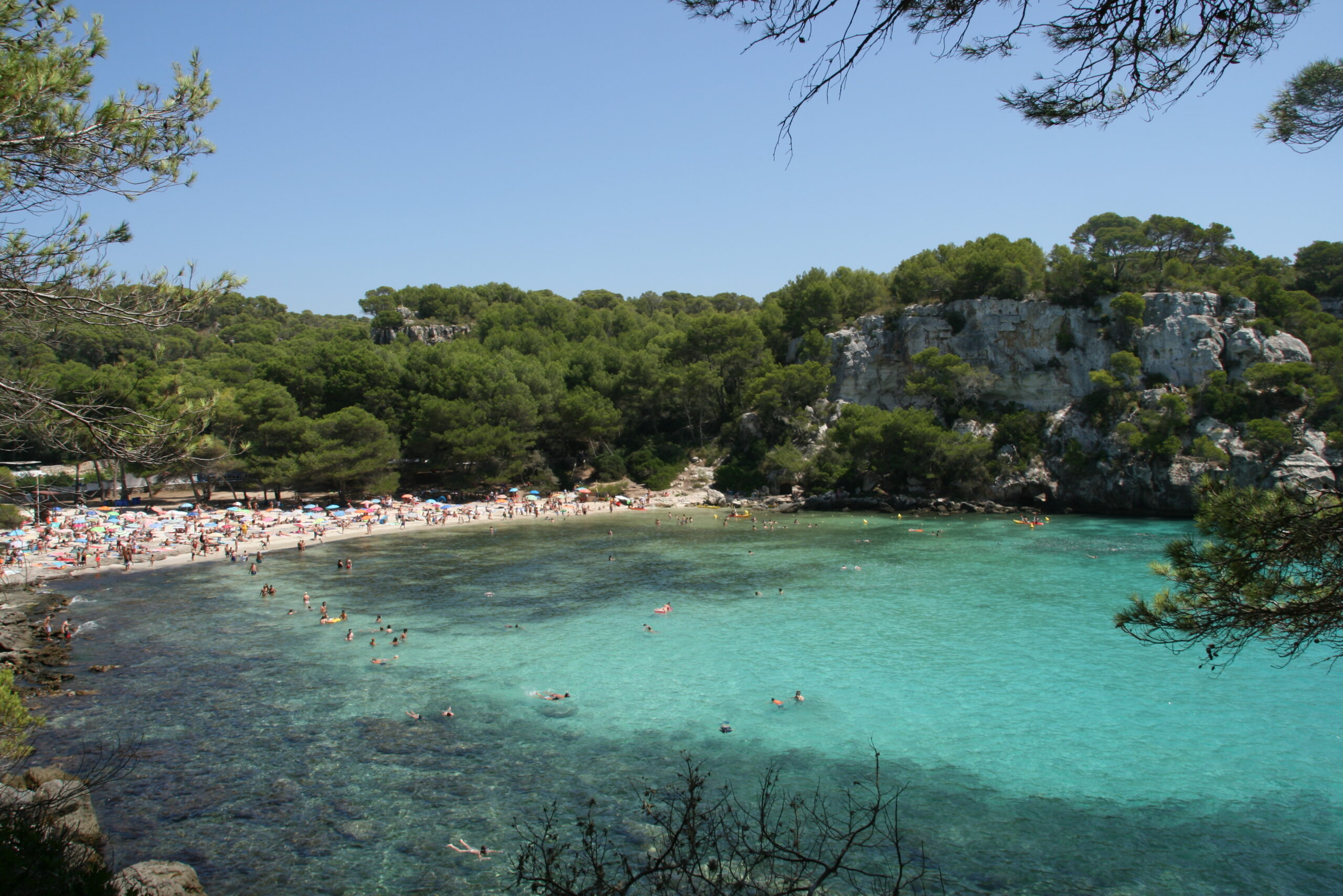 Menorca in augustus: het warmste water en de festes 2 Cala Macarella op Menorca met een vol strand, zwemmers en turquoise water begin augustus