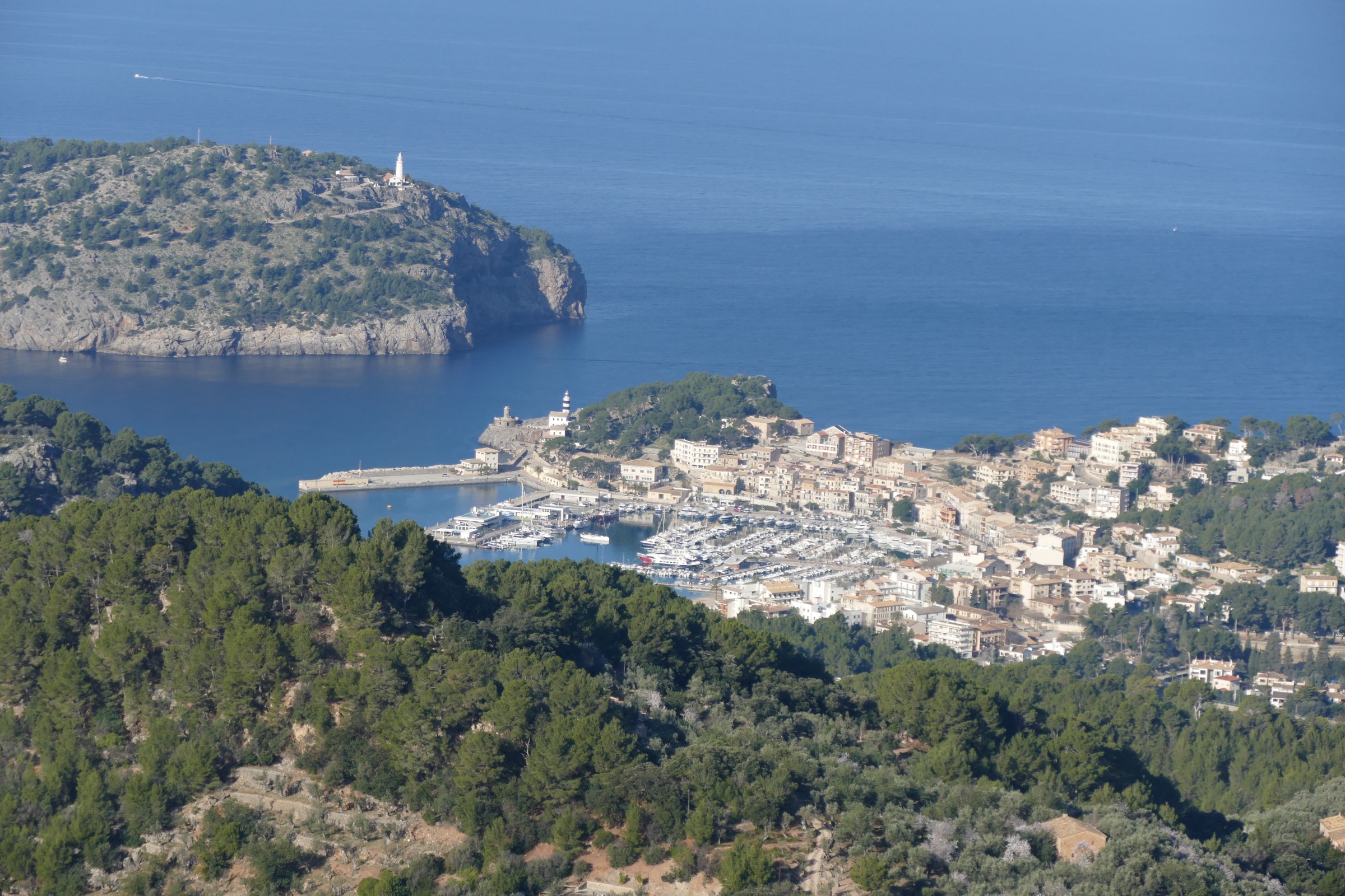 Mirador de ses Barques: het uitzichtpunt boven Port de Sóller 3 Port de Sóller gezien vanaf Mirador de ses Barques in de winter, met de vuurtoren op de kaap, de havenpier en bloeiende amandelbomen op de voorgrond