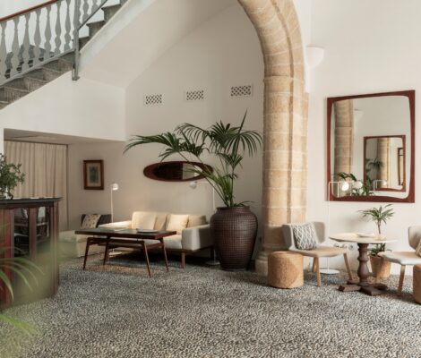 De hoge hal van restaurant Mouna in Palma met een stenen boog, een trap met gedraaide balustrade, een vloer van kiezelmozaïek en lichte fauteuils