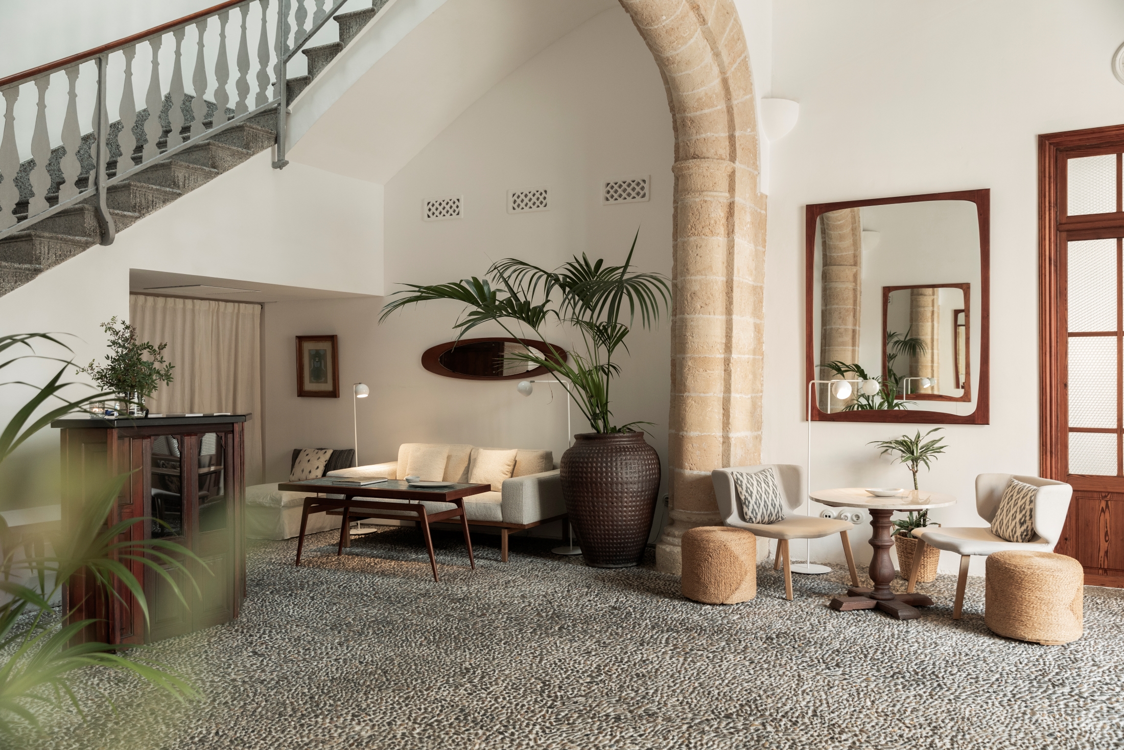 Mouna Palma: 100% biologisch vegetarisch eten in een oud casal 1 De hoge hal van restaurant Mouna in Palma met een stenen boog, een trap met gedraaide balustrade, een vloer van kiezelmozaïek en lichte fauteuils
