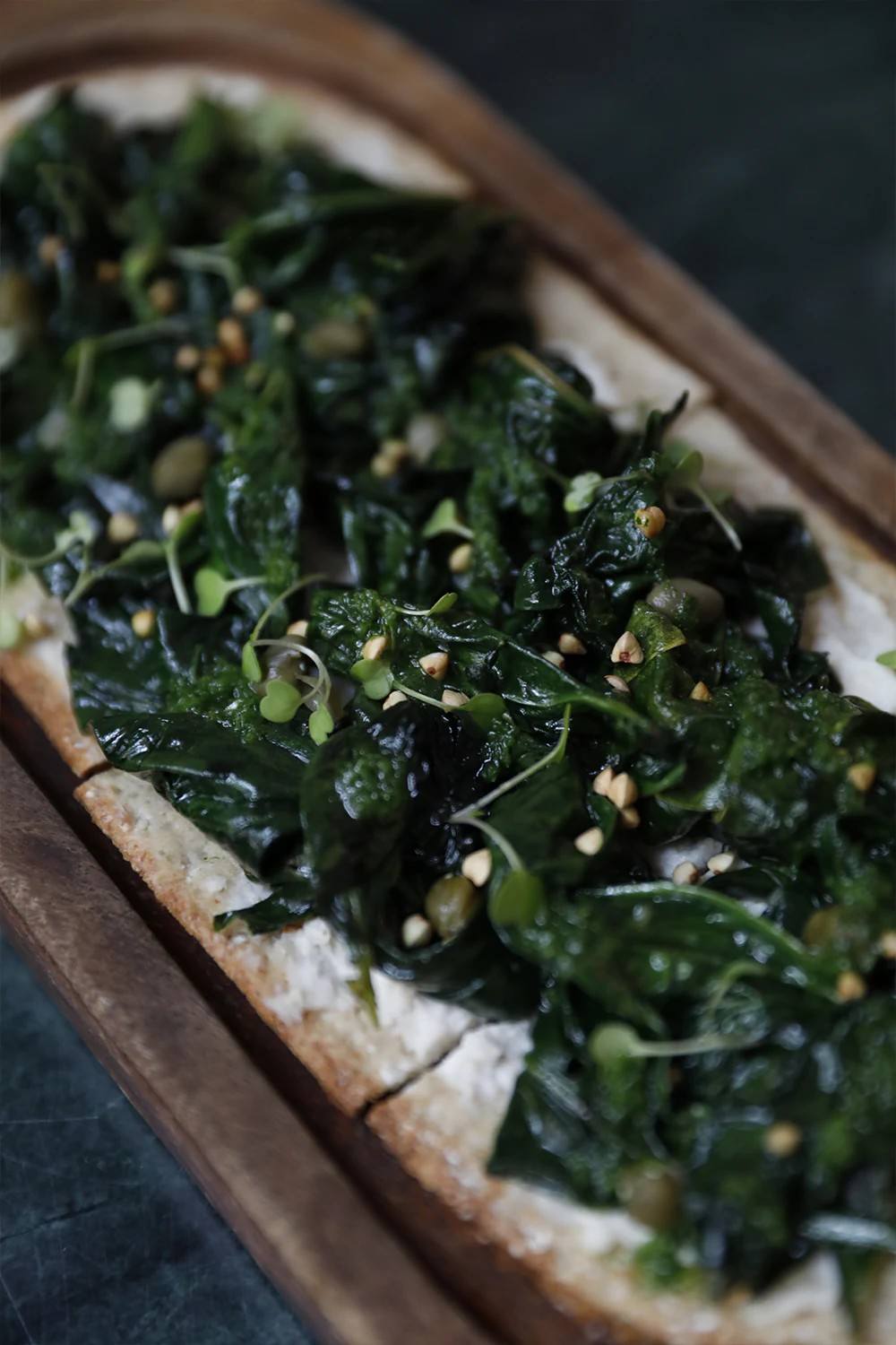 Mouna Palma: 100% biologisch vegetarisch eten in een oud casal 4 Een Mallorcaanse coca met spinazie, kappertjes en pijnboompitten op een langwerpige houten plank bij Mouna in Palma