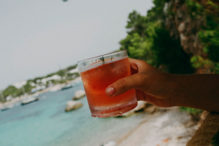 Hand met een cocktail boven de baai van Portinatx