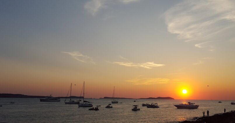 Zonsondergang bij Sant Antoni op Ibiza met excursieboten en een boot vol passagiers voor de kust