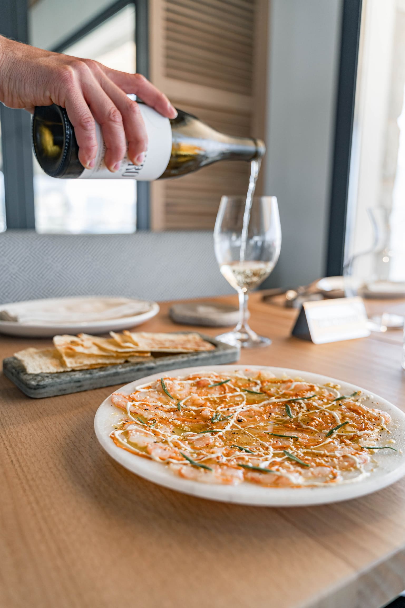 Periplo Portixol (Palma): vis van de grill aan het water in es Molinar 5 Carpaccio van rode garnaal met kruidenolie op een rond bord bij Periplo Portixol, met krokant brood ernaast en wijn die wordt ingeschonken