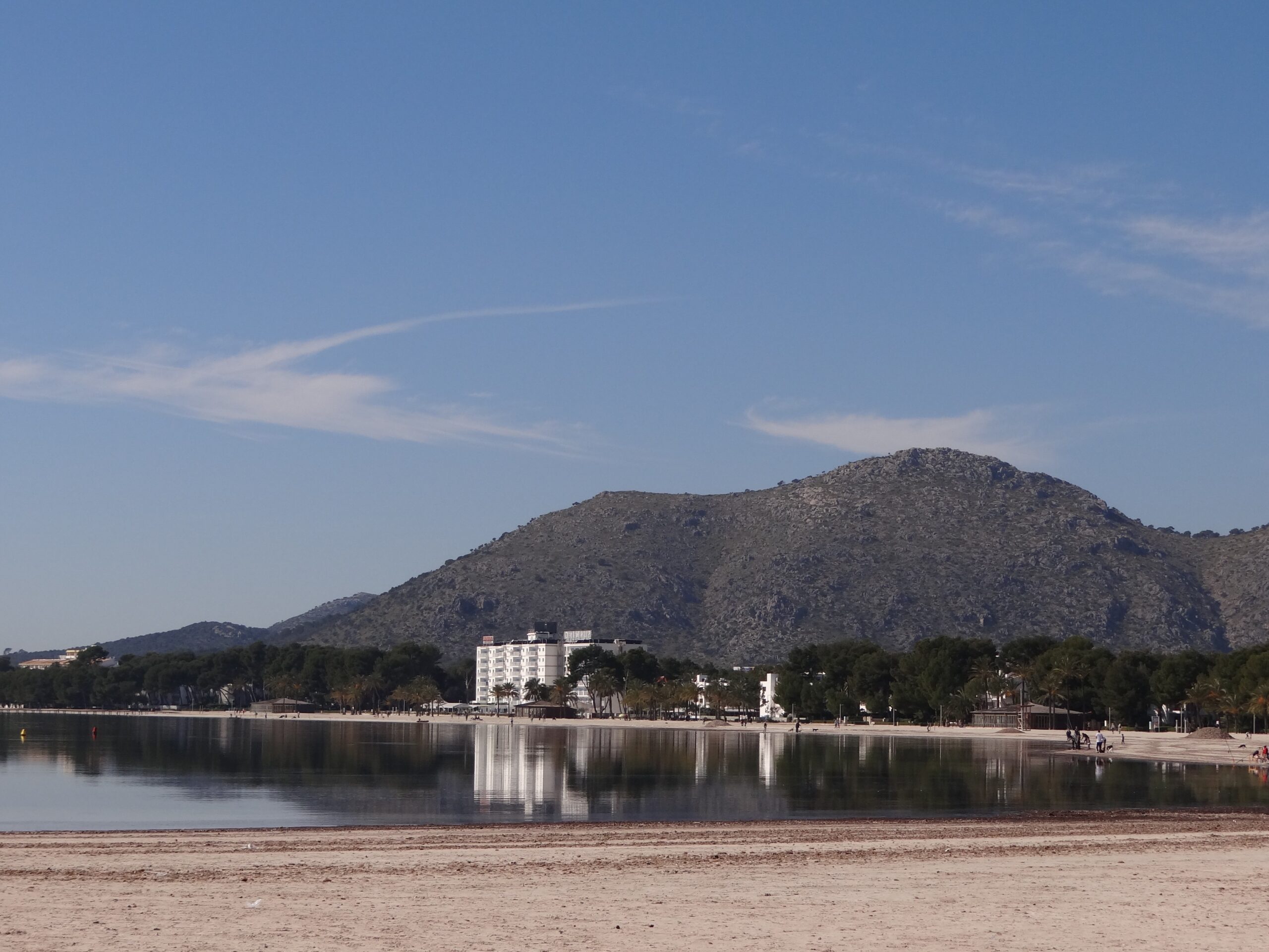 Platja d'Alcúdia: 3,4 kilometer zand en ondiep water in de baai van Alcúdia 5 Spiegelglad water aan de noordkant van Platja d'Alcúdia op een windstille ochtend, met de hotels en een beboste berg weerspiegeld in de zee