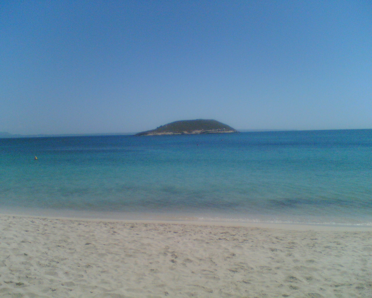 Het ondiepe, heldere water van Magaluf met de lichte zandbodem zichtbaar tot ver in zee en een eilandje aan de horizon
