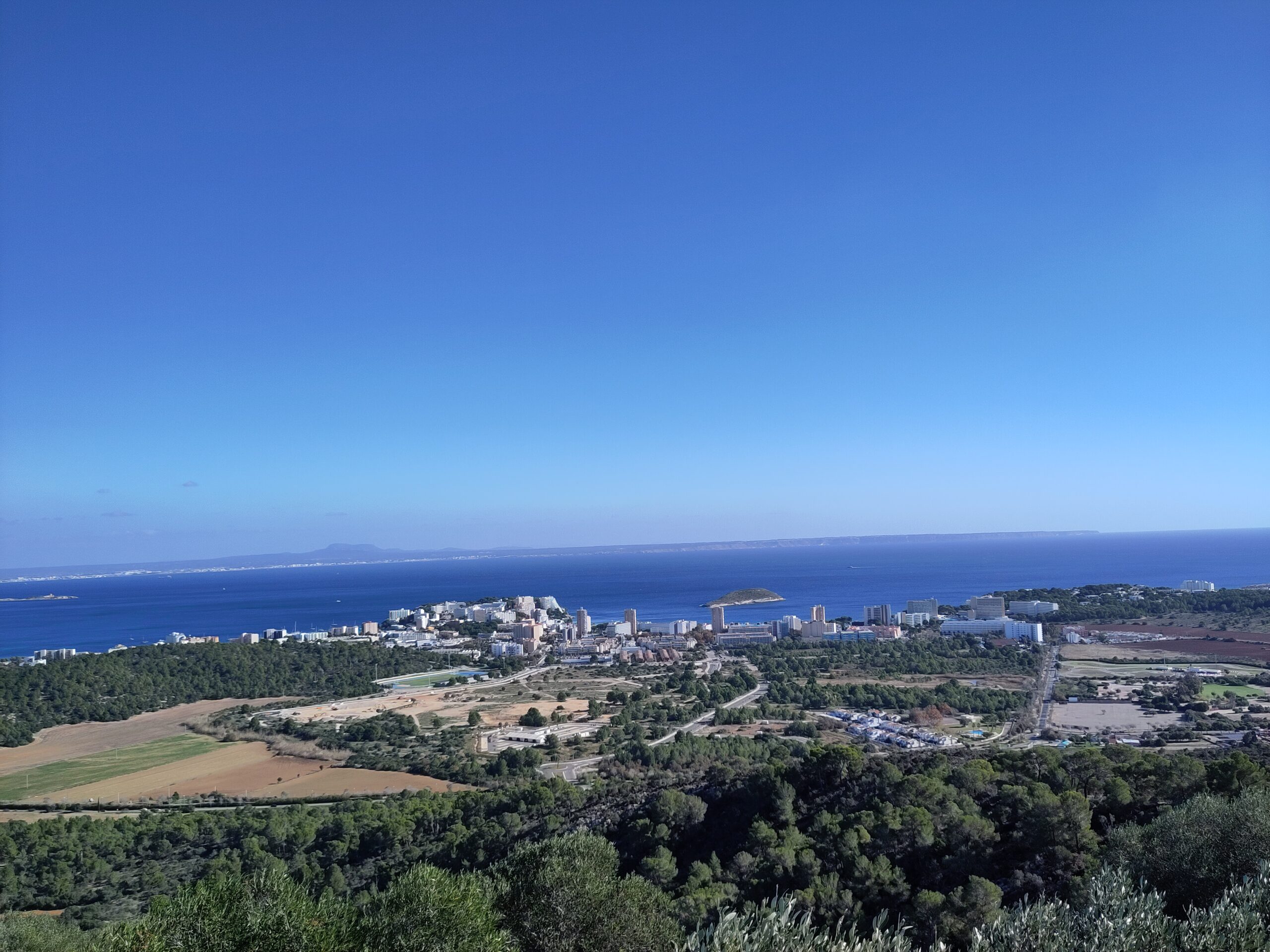 Magaluf gezien vanaf het Puig d'en Saragossa, met de hotelbebouwing aan de kust, het groene achterland ervoor en de baai van Palma erachter
