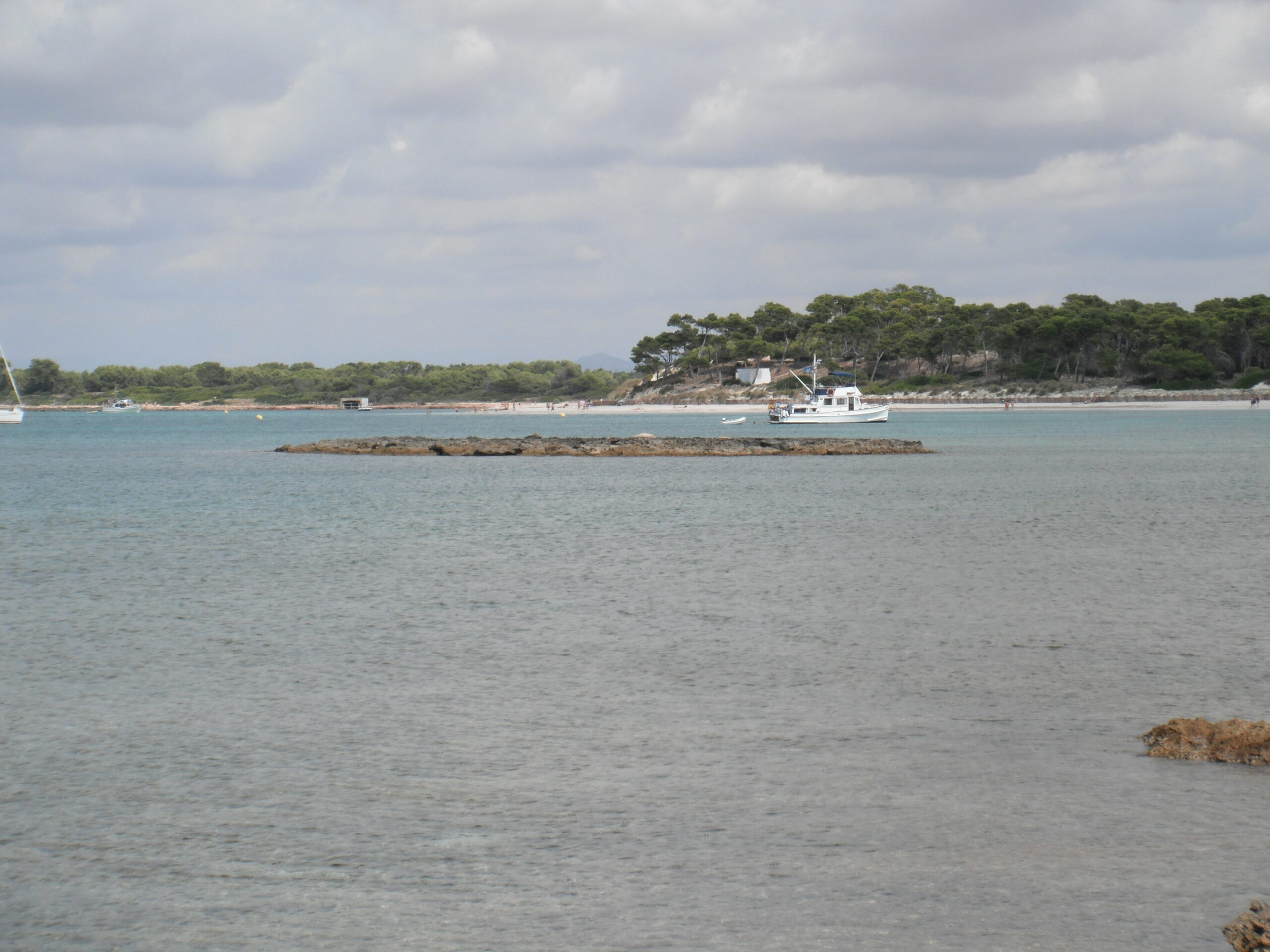 Platja des Carbó Mallorca: onbebouwd wit zand bij Colònia de Sant Jordi 4 De lage rotsplaat van de Illot de ses Roquetes voor de kust van Es Carbó, met op de achtergrond het witte strand, het dennenbos en een paar ankerende boten
