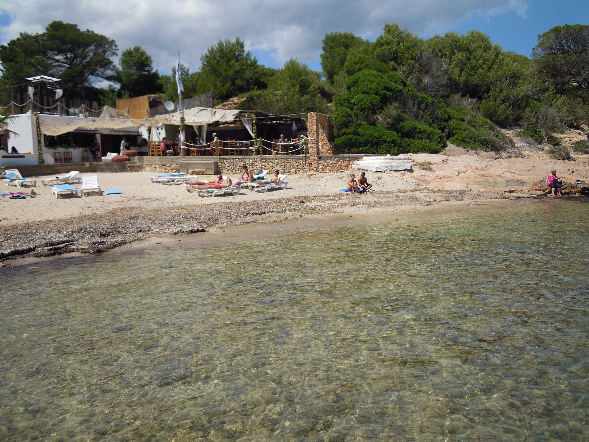Platja de s’Estanyol Ibiza: de rotsbaai bij Cap Martinet 4 De smalle strook zand bij s'Estanyol met ligbedden voor het strandrestaurant en helder ondiep water
