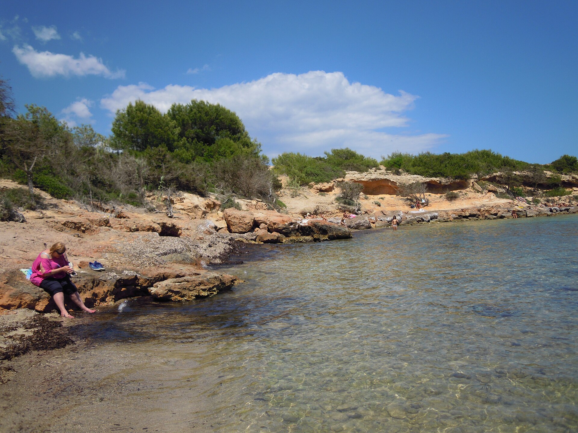 Platja de s’Estanyol Ibiza: de rotsbaai bij Cap Martinet 1 De ockerkleurige rotsplaten van Platja de s'Estanyol met kristalhelder ondiep water ervoor en pijnbomen op de rand