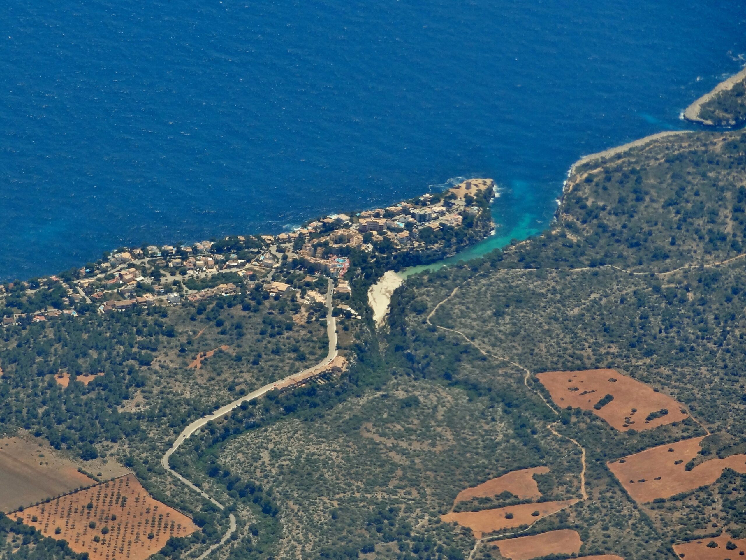 Luchtfoto van de zuidkust van Mallorca waarop de smalle kloof van Cala Pi tussen de vlakke kliffen het land in snijdt, met akkers en pijnbos eromheen