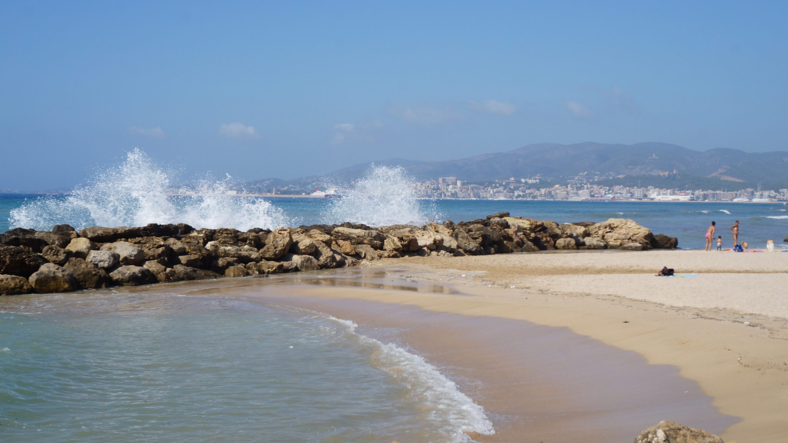 Playa de Palma (Mallorca): het grote stadsstrand bij Palma 6 Golven die breken op de stenen golfbreker bij Can Pastilla, met het zand van de Playa de Palma en de baai van Palma erachter