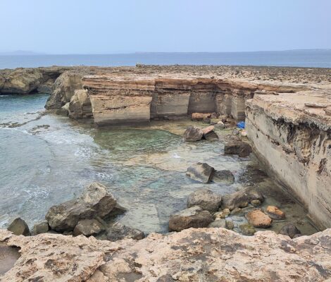 De uitgehakte wanden van de oude steengroeve bij Punta de sa Pedrera op Formentera, met de ondergelopen vloer en Ibiza aan de horizon