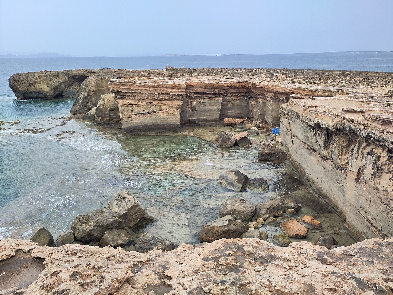 De uitgehakte wanden van de oude steengroeve bij Punta de sa Pedrera op Formentera, met de ondergelopen vloer en Ibiza aan de horizon