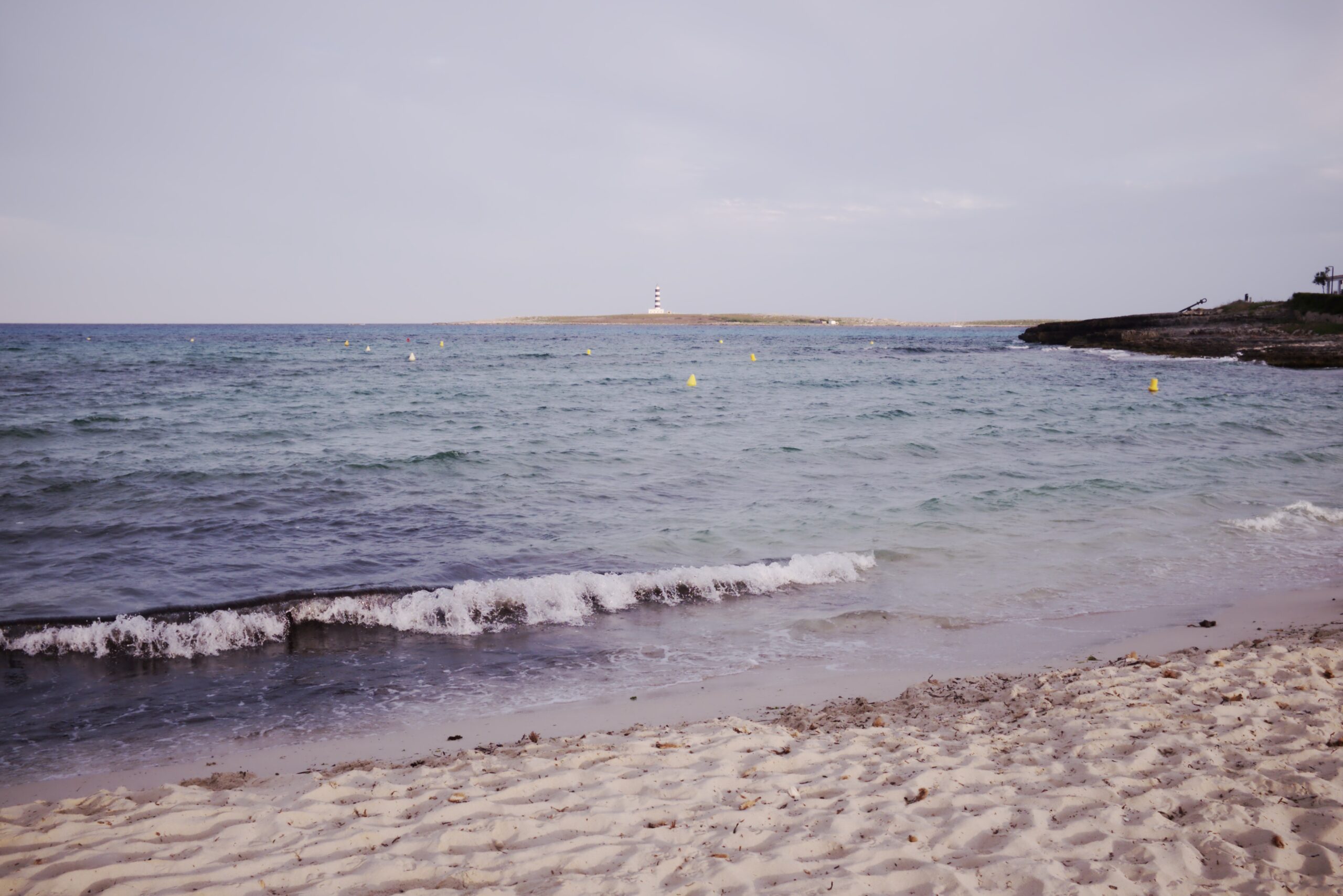 Het witte zand van Punta Prima op Menorca met het eilandje Illa de l'Aire en zijn gestreepte vuurtoren aan de horizon