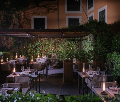De tuin van restaurant Quadrat in Palma bij avond, met gedekte tafels onder een pergola en kaarslicht tussen het groen
