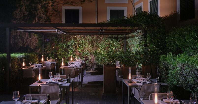 De tuin van restaurant Quadrat in Palma bij avond, met gedekte tafels onder een pergola en kaarslicht tussen het groen