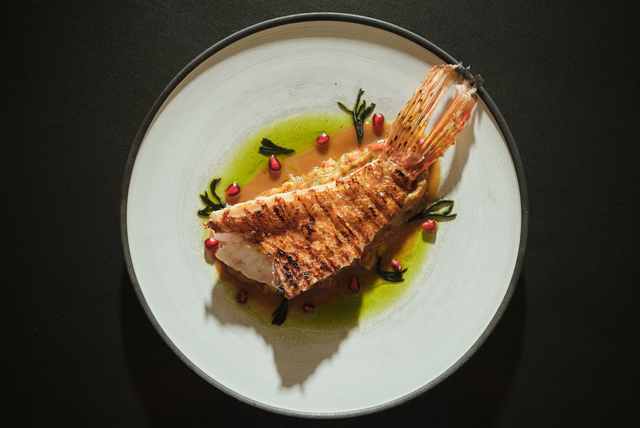 Quadrat in Palma: eten in de tuin van Hotel Sant Francesc 8 Een hele vis van de grill in groene kruidenolie op een wit bord, een gerecht van restaurant Quadrat in Palma