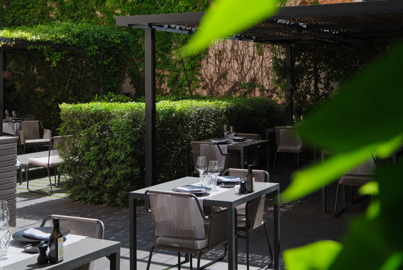 Quadrat in Palma: eten in de tuin van Hotel Sant Francesc 4 De tuin van Quadrat overdag, met tafels onder een pergola tussen hoge hagen en klimop